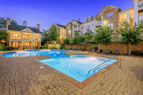 A swimming pool surrounded by a brick patio at dusk.
